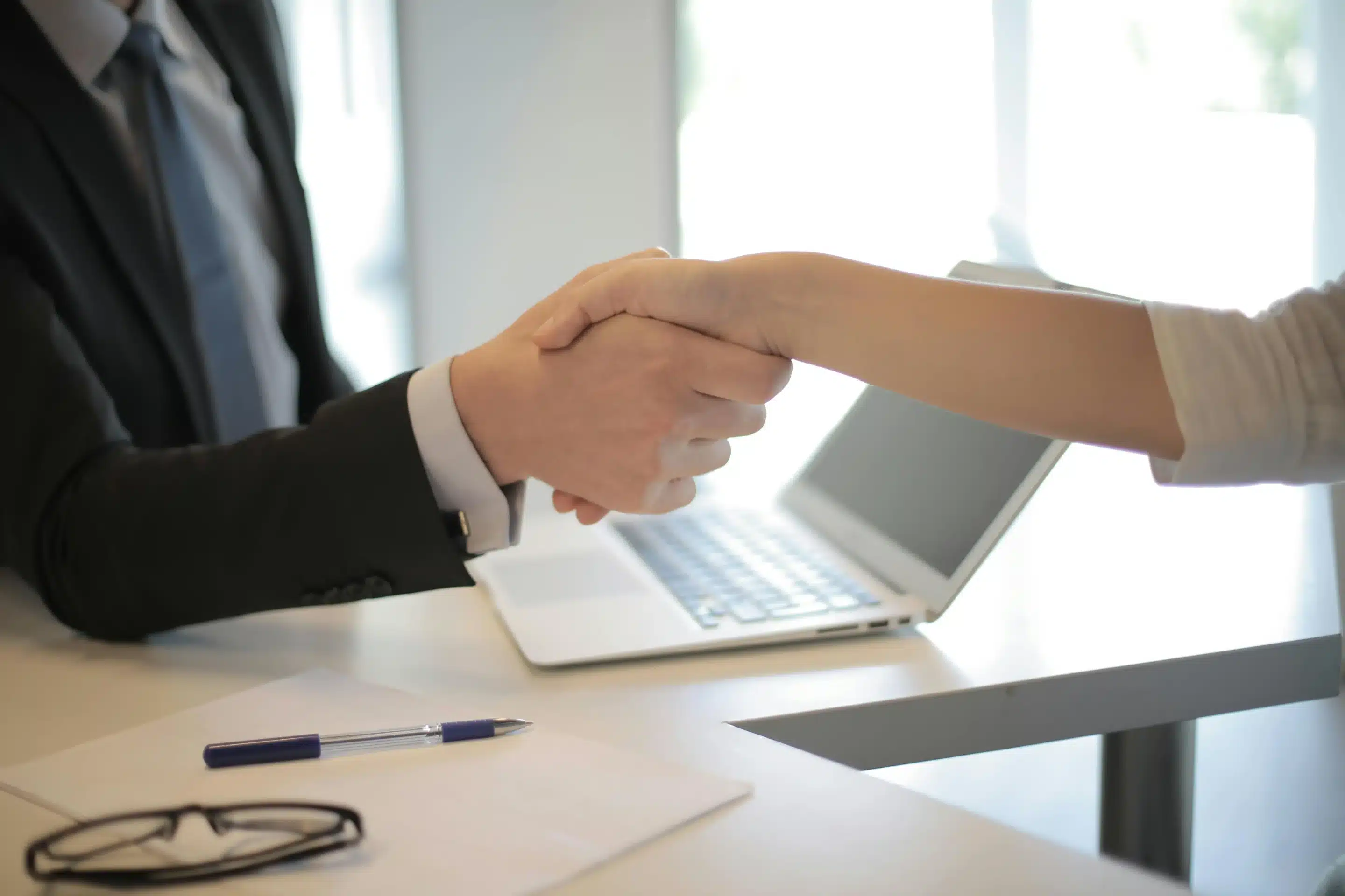 Medical Billing Outsourcing: The Pros & Cons Two people shaking hands, with a laptop in the background. The setting looks like a business meeting.