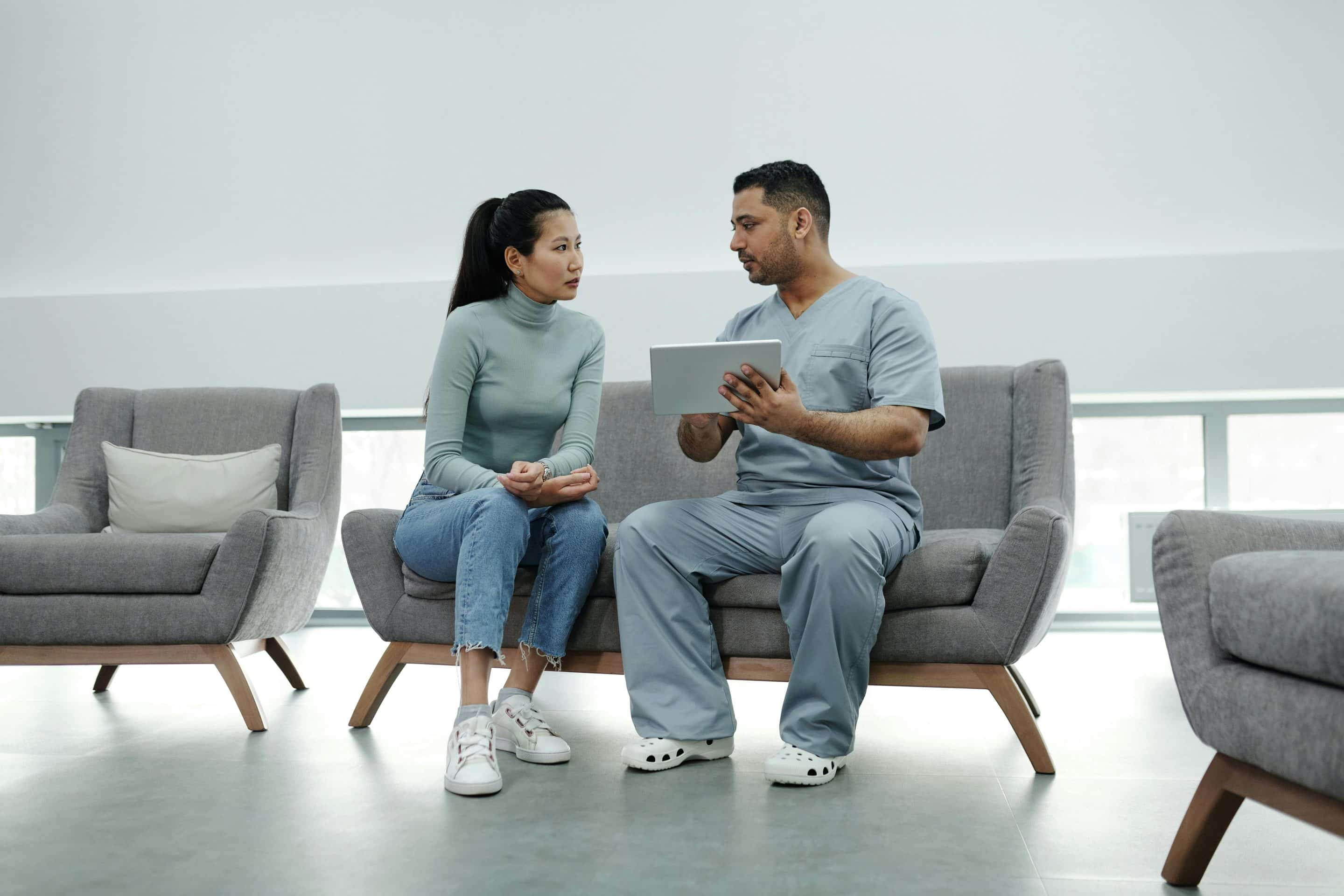 Doctor sitting next to patient on a couch with a clipboard